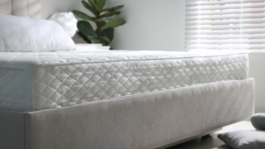 A close-up of a neatly made bed with a white mattress in a bright, modern bedroom.